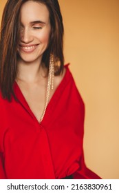 Girl in red shirt with puff sleeves, gold earrings and dark grey pants. Fashion studio portrait of young elegant woman wear minimalists outfit. Short hair brunette woman. Girl smiling and laughing.