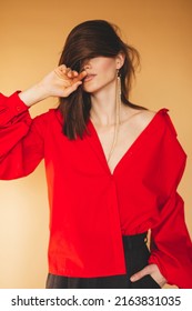 Girl in red shirt with puff sleeves, gold earrings and dark grey pants. Fashion studio portrait of young elegant woman wear minimalists outfit. Short hair brunette woman looks proud and sensual.