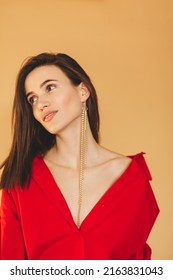 Girl in red shirt with puff sleeves, gold earrings and dark grey pants. Fashion studio portrait of young elegant woman wear minimalists outfit. Short hair brunette woman looks happy and laughing.