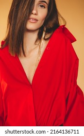 Girl in red shirt with puff sleeves, gold earrings and dark grey pants. Fashion studio portrait of young elegant woman wear minimalists outfit. Short hair brunette woman.