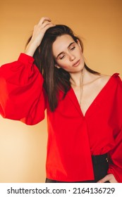 Girl in red shirt with puff sleeves, gold earrings and dark grey pants. Fashion studio portrait of young elegant woman wear minimalists outfit. Short hair brunette woman looks proud and sensual.