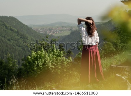 Girl in red skirt on viewpoint looking on mountains holding her hair 