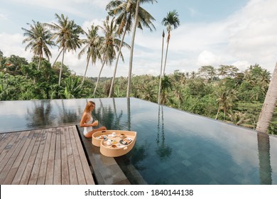 Girl relaxing and eating floating breakfast served in heart shaped rattan tray  in jungle pool on luxury villa in Bali. Valentines day or honeymoon surprise. Tropical travel lifestyle