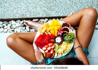 Girl Relaxing And Eating Fruit Plate By The Hotel Pool. Exotic Summer Diet. Photo Of Legs With Healthy Food By The Poolside, Top View From Above. Tropical Beach Lifestyle.