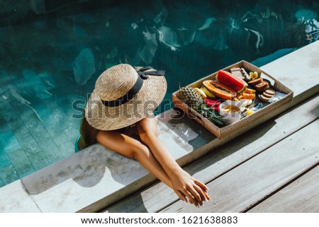 Girl relaxing and eating fruits in the pool on luxury villa in Bali. Exotic summer diet. Tropical beach lifestyle.