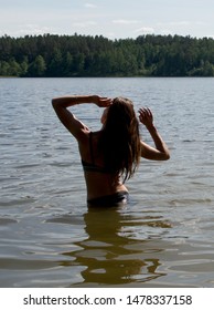 Girl Relaxing In The Lake With Arms Up. Freedom And Adventure Concept.Woman In Black Bikini Posing In The Water. Romantic Woman. Caucasian White Woman. Summer Holidays. Sunset Hours. Woman Swiming