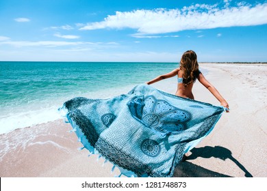 Girl relaxing on the beach, looking at sea landscape and holding boho pareo on the wind