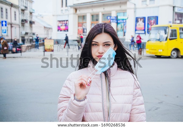 Girl remove mask from the face on the street.\
Danger. Te end of epidemic. COVID-19 Pandemic Coronavirus Young\
girl in city street wearing face mask protective for spreading of\
Coronavirus Disease 2019