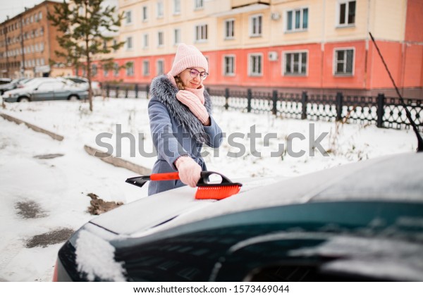 girl removes snow from the car. girl in a coat on\
the street