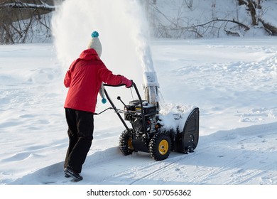 Girl removes snow with gas snow thrower at winter day.