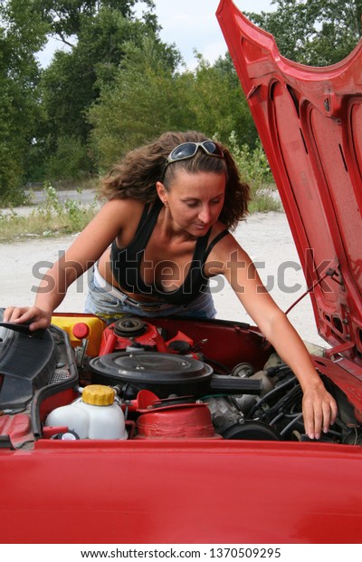 The\
girl repairs the car. Young woman near the red\
car.