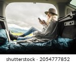 Girl resting in her car with her phone. Woman hiker, hiking backpacker traveler camper in sleeping bag relaxing on top of mountain. Road trip, Health care, authenticity, sense of balance and calmness.