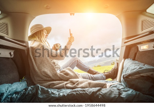 Girl resting in her car with her phone. Woman\
hiker, hiking backpacker traveler camper in sleeping bag relaxing\
on top of mountain. Road trip, Health care, authenticity, sense of\
balance and calmness.