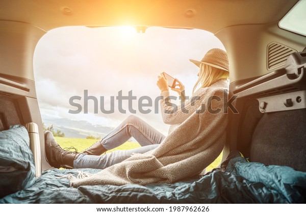 Girl resting in her car with her phone. Woman\
hiker, hiking backpacker traveler camper in sleeping bag relaxing\
on top of mountain. Road trip, Health care, authenticity, sense of\
balance and calmness.