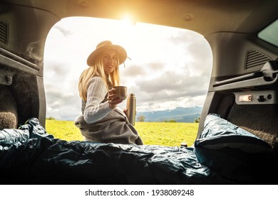 Girl Resting In Her Car. Woman Hiker, Hiking Backpacker Traveler Camper In Sleeping Bag, Relaxing, Drinking Hot Tea On Top Of Mountain. Road Trip. Health Care, Authenticity, Sense Of Balance Calmness.