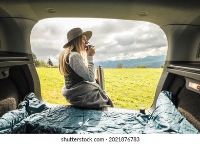 Girl Resting In Her Car. Woman Hiker, Hiking Backpacker Traveler Camper In Sleeping Bag, Relaxing, Drinking Hot Tea On Top Of Mountain. Road Trip. Health Care, Authenticity. Fall Style