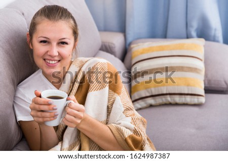 Girl is resting with tea in plaide at home.