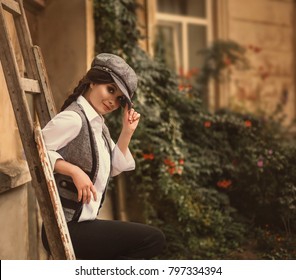 Girl Retro Hooligan. Woman Like Man. The Peaky Blinders. Vintage Style. Times Great Depression. Clothes Shirt Suspenders Black Pants, Gray Vest, Pretty Face, Hat Cap.old House Wooden Staircase, Flower