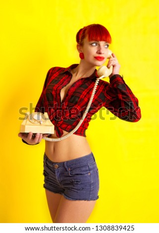 The girl in retro style, in a bright checkered shirt tied on the stomach and shorts talking on the phone on a bright yellow background
