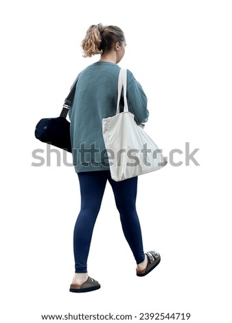 A girl returns from a yoga class at the gym. She is holding a bag with sports clothes and a yoga mat. Cut out young woman pedestrian in tights and slippers. Back view of female athlete in motion