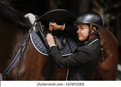 Girl rider adjusts saddle on her horse to take part in horse races. - Powered by Shutterstock