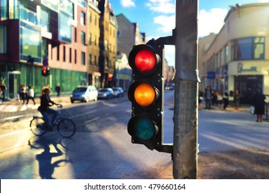 Girl rides on the street on a bicycle among the cars in the city center in a beautiful light by a traffic light with red and orange