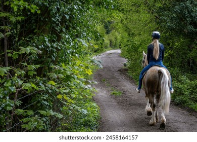 Girl riding a horse down a quiet country road, Image shows a young blonde girl in her 20's hacking out her section D Welsh cob stallion down a quiet country lane on a warm spring day - Powered by Shutterstock