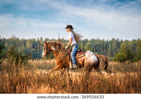 Girl riding on the Appaloosa horse on the field in the tall yellow grass trees and sky background