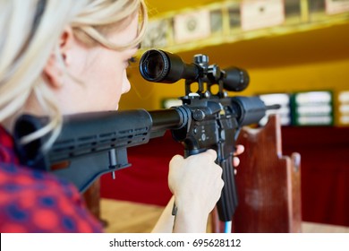 Girl with rifle aiming at target during shooting practice
