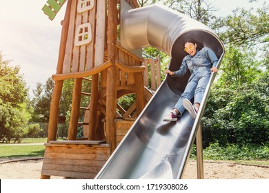 A girl rolls down a steep children's slide on the Playground. Concept of infantilism and personal psychology - Powered by Shutterstock