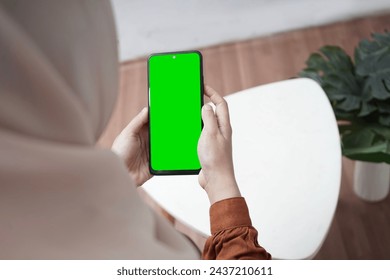 Girl in the room holding a smartphone with a green screen, with a table beside her - Powered by Shutterstock