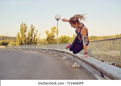 A girl runner jumps over a railing on a bridge in the city. - Shutterstock ID 711466099