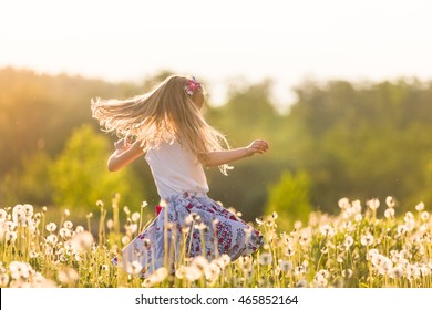 Girl running on the field of dandelions on sunset. Beautiful little kid dancing on dandelion meadow. Summer fun outdoors.