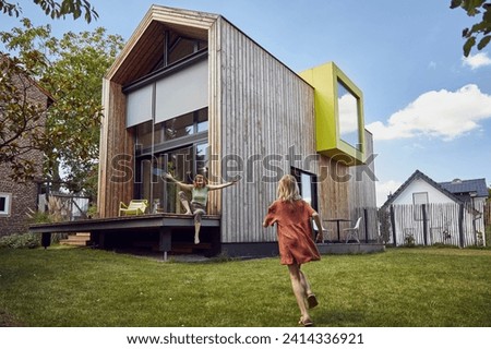 Girl running towards happy mother sitting outside tiny house
