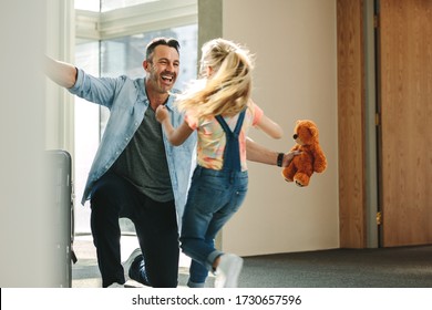 Girl running towards her father at the entrance door holding a teddy bear. Daughter meeting her father just arrived from a business trip. - Powered by Shutterstock