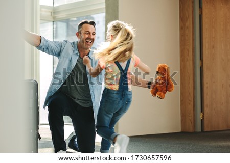 Girl running towards her father at the entrance door holding a teddy bear. Daughter meeting her father just arrived from a business trip.