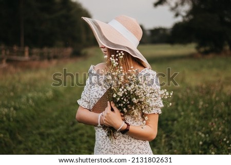 the girl runs across the field. Happy girl. Long hair. White dress. A hat with a brim. Bouquet of daisies. A young girl in nature.