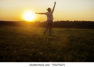 the girl runs against the sunset in jeans and a white T-shirt. sunset against the background of the forest. summer. heat. happiness. joy. sunset. sunrise. yellow. Orangesunrise. yellow. Orange