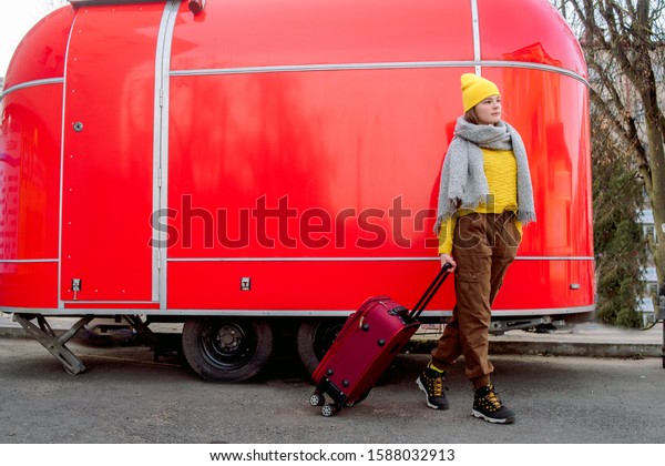 girl runs\
with a red suitcase on a red background. Large retro vintage van.\
Old car. Traveling in the winter. Girl in a yellow bright hat and\
knitted sweater. Travel concept.copy\
space
