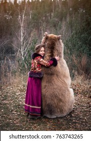 A girl in the Russian national dress hugging a real brown big bear. Lte autumn period in the forest 