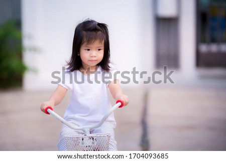 Girl is sadly riding bicycle from social distancing in epidemic pneumonia situation. She doesn't have friends of the same age to run around and talk to. Asian children lonely and depressed.