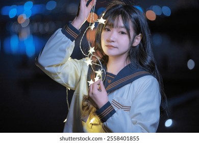 A girl in a sailor-style outfit holds illuminated star-shaped string lights at night, with blurred city lights in the background. - Powered by Shutterstock