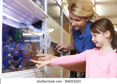 Girl With Sales Assistant Choosing Goldfish In Pet Store