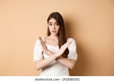 Girl Says No. Skeptical Young Woman Disagree Or Prohibit Action, Showing Cross Stop Gesture, Make Nope Sign, Disapprove Bad Idea, Standing On Beige Background