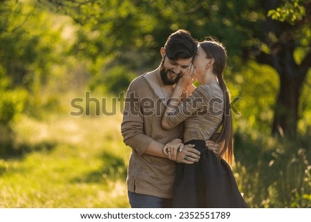 girl says something in the ear of her boyfriend, walking in nature
