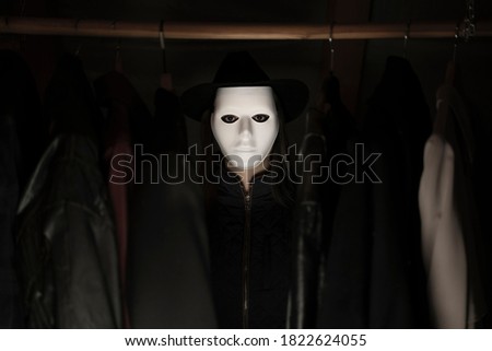 A girl in a scary white mask and black hat. Hiding in the closet. Scary horror concept.