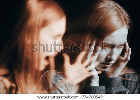Girl with schizophrenia covering her ears to not hear the voice of her alter ego. Blurred person