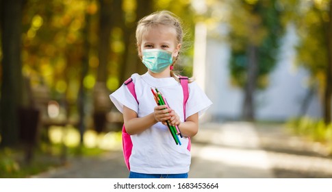 Girl In School Uniform With Air Pollution Mask On Face, Looks At Camera Standing In Front Of School