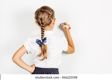 girl in a school uniform writing something on board with a marker. Learning and school concept. Image on white background.