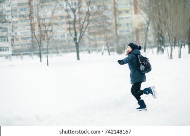 Girl Schoolgirl With A School Backpack Over Her Shoulders Runs To School. Child In The Background Of A School In Winter.